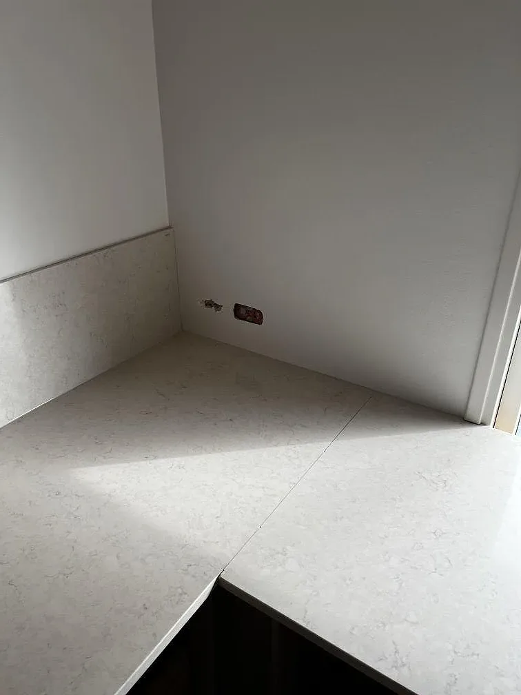 Polerad kompositsten Silestone Snowy Ibiza med matchande väggparti och bänkyta i kök under montering i Dyssegård.