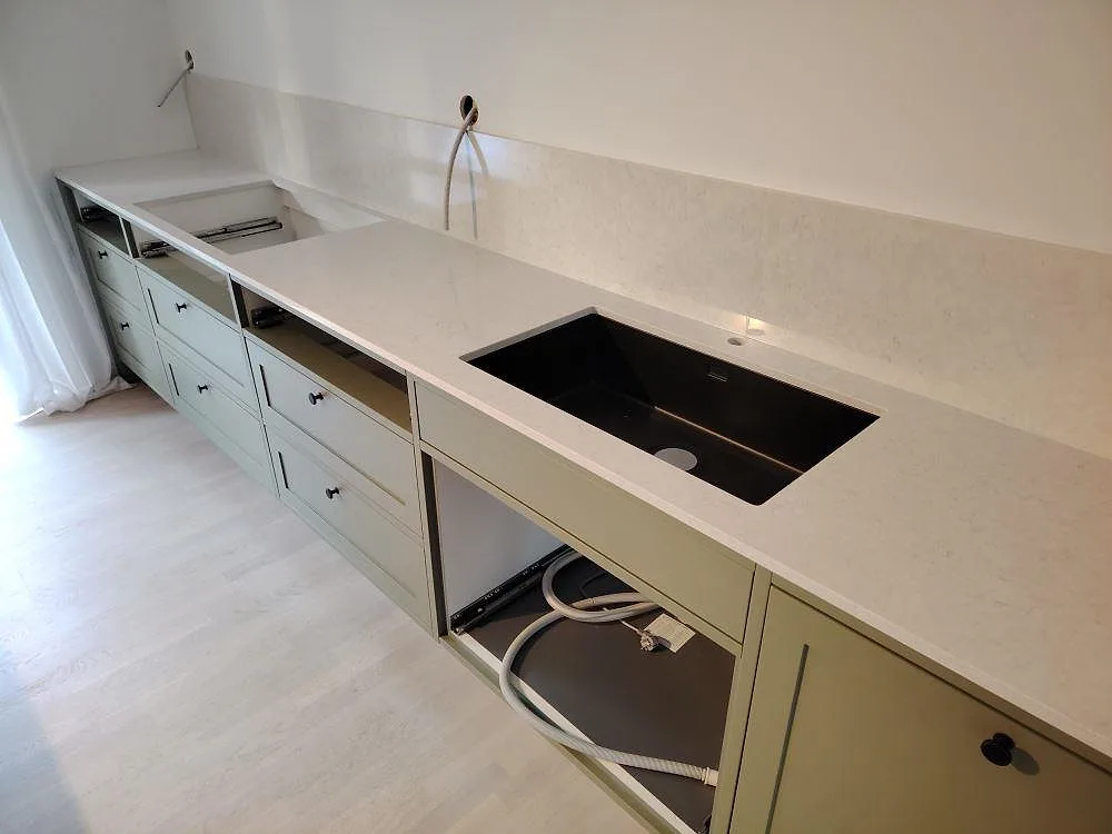 Närbild av väggbänk i polerad Silestone Snowy Ibiza, kvartskomposit, med mörk diskho, låg stänkkant och ljus ådring i Ekerö.