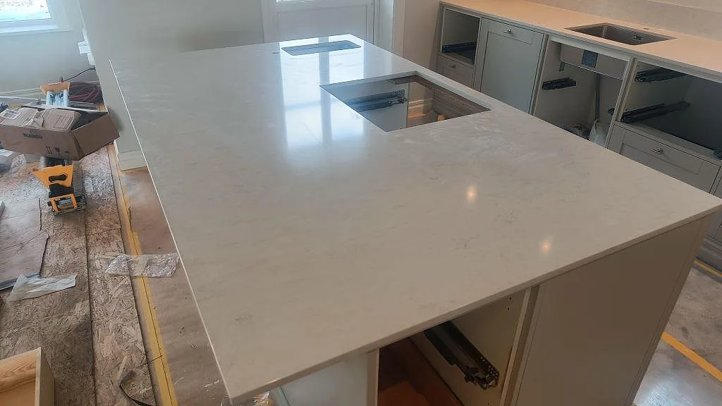 Polerad bänkskiva i Silestone Snowy Ibiza på köksö med hällöppning och ljusa skåpsstommar under montering i Ellös.