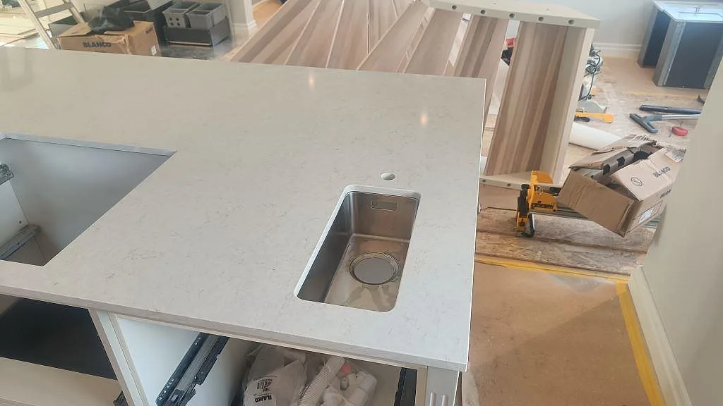 Detaljbild av köksö i Silestone Snowy Ibiza med underlimmad rostfri diskho och kranhål under montering i Ellös.