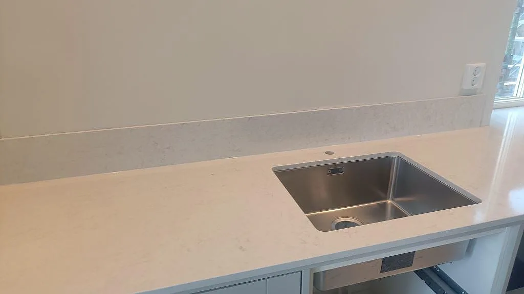 Köksbänk i polerad Silestone Snowy Ibiza med låg stänkkant och underlimmad rostfri diskho vid fönster i Ellös.