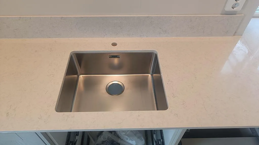 Närbild på underlimmad rostfri diskho i polerad Silestone Snowy Ibiza med låg stänkkant i kök i Ellös.