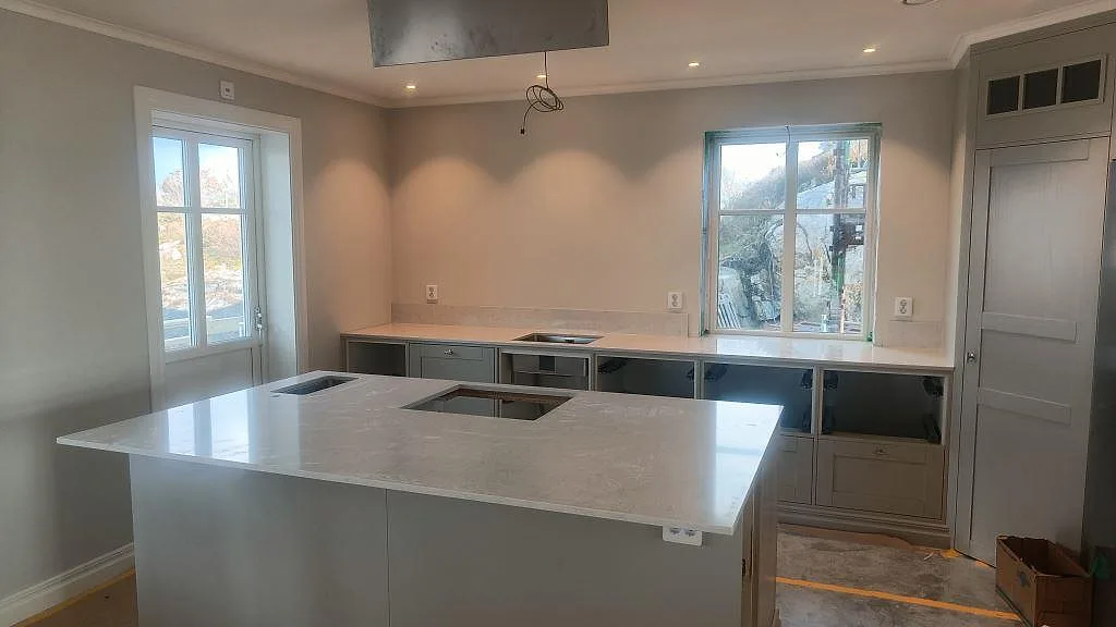 Köksbänkskiva i polerad Silestone Snowy Ibiza med stor köksö, hällöppning och underlimmade rostfria hoar i ett kök i Ellös.