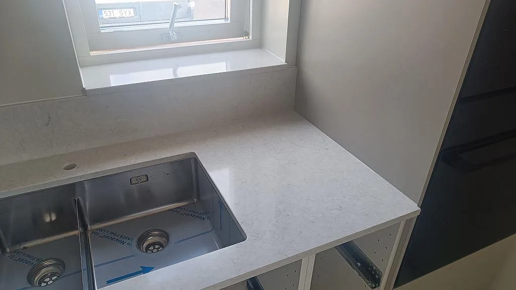 Polerad kompositbänkskiva i Silestone Snowy Ibiza vid diskho och fönsterbänk under köksmontering i Falkenberg.