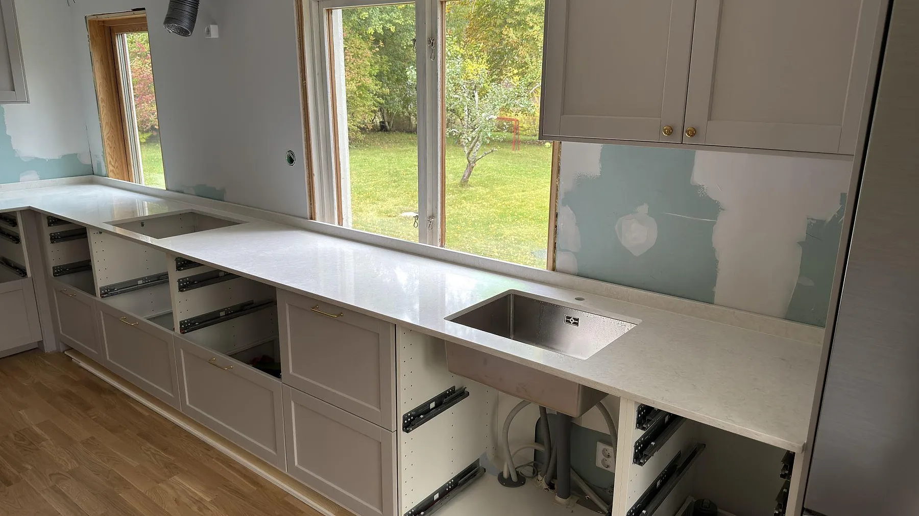 Polerad köksbänkskiva i Silestone Snowy Ibiza med rostfri diskho, öppna köksstommar och ljus stänkkant under fönster i Farsta.