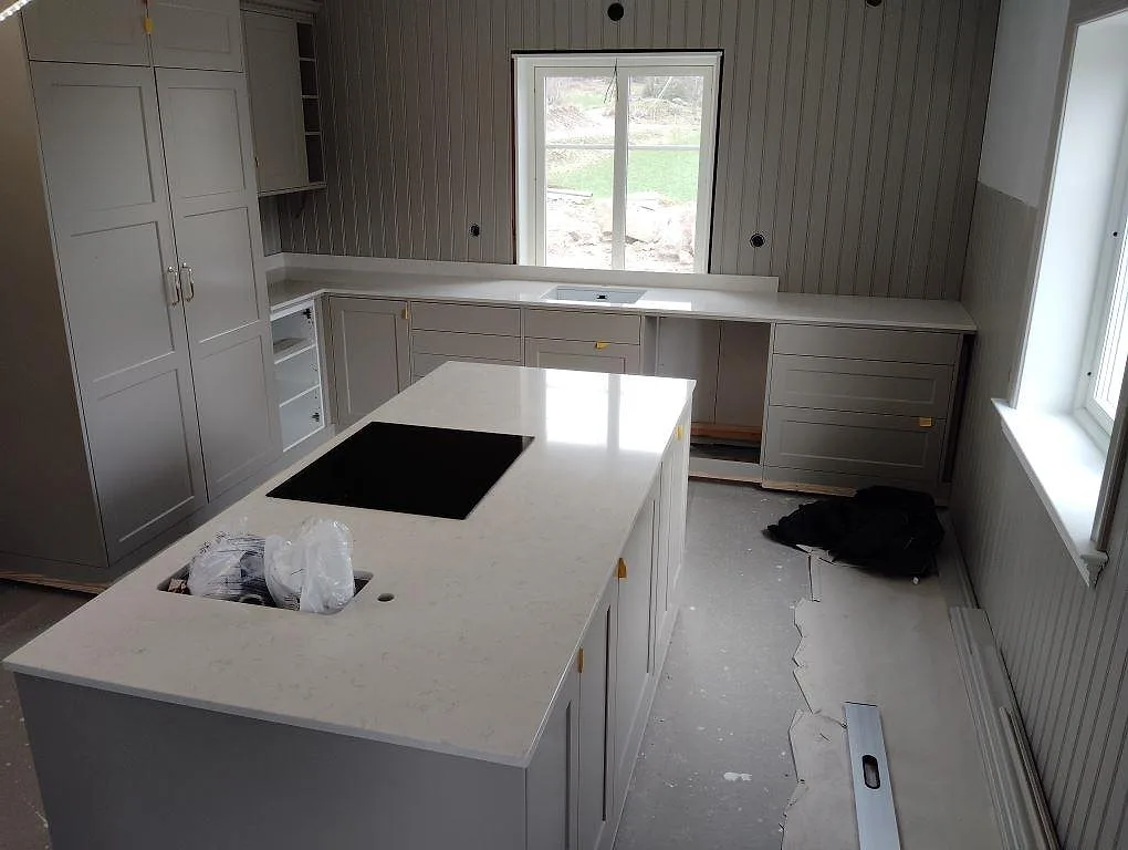 Polerad köksbänkskiva i vit Silestone Snowy Ibiza med köksö, häll och bänklängd under fönster i ett kök i Finspång.