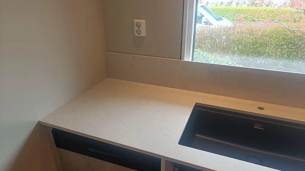 Bänkskiva i polerad Silestone Snowy Ibiza med svart diskho, blandarhål och låg stänkkant vid fönster i Fjärås.