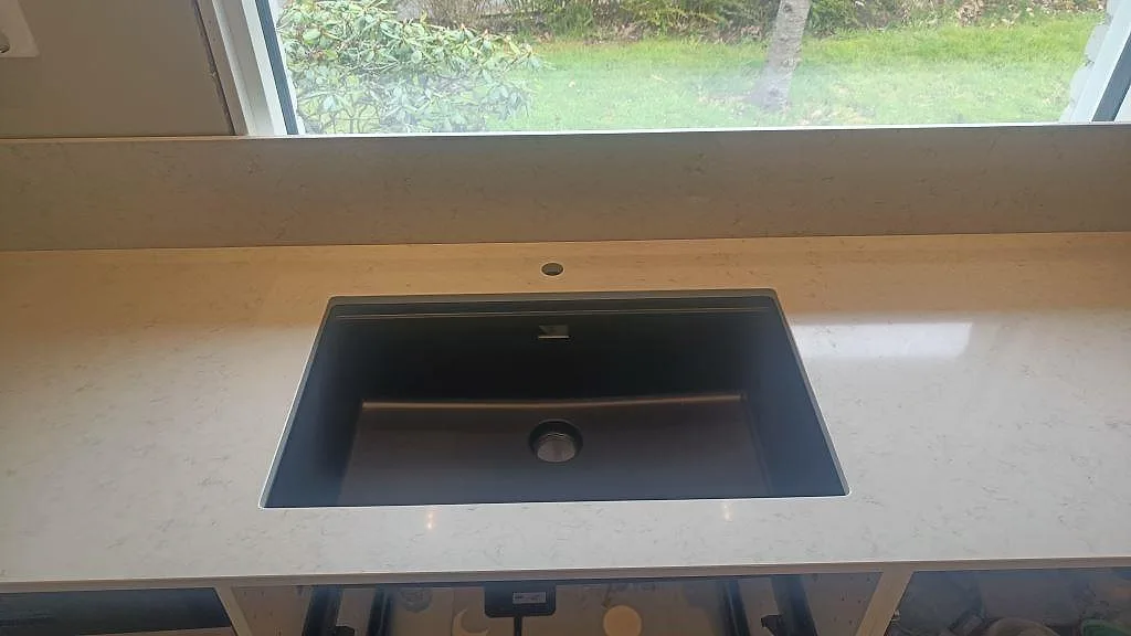 Svart underlimmad diskho i polerad Silestone Snowy Ibiza med 12 mm stänkskydd under fönster i ett kök i Fjärås.