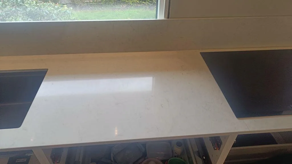 Perimeterbänk i polerad Silestone Snowy Ibiza mellan svart diskho och svart häll med stänkskydd under fönster i Fjärås.