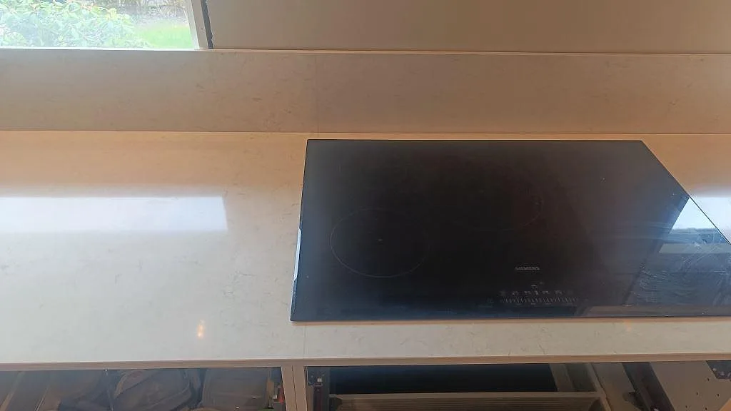 Svart häll monterad i polerad Silestone Snowy Ibiza med matchande stänkskydd och ljus bänkskiva i Fjärås.