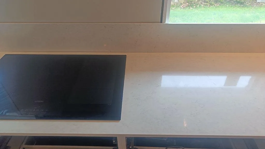 Detalj av svart häll och blank Silestone Snowy Ibiza bänkskiva med fönsterljus och stänkkant i Fjärås.