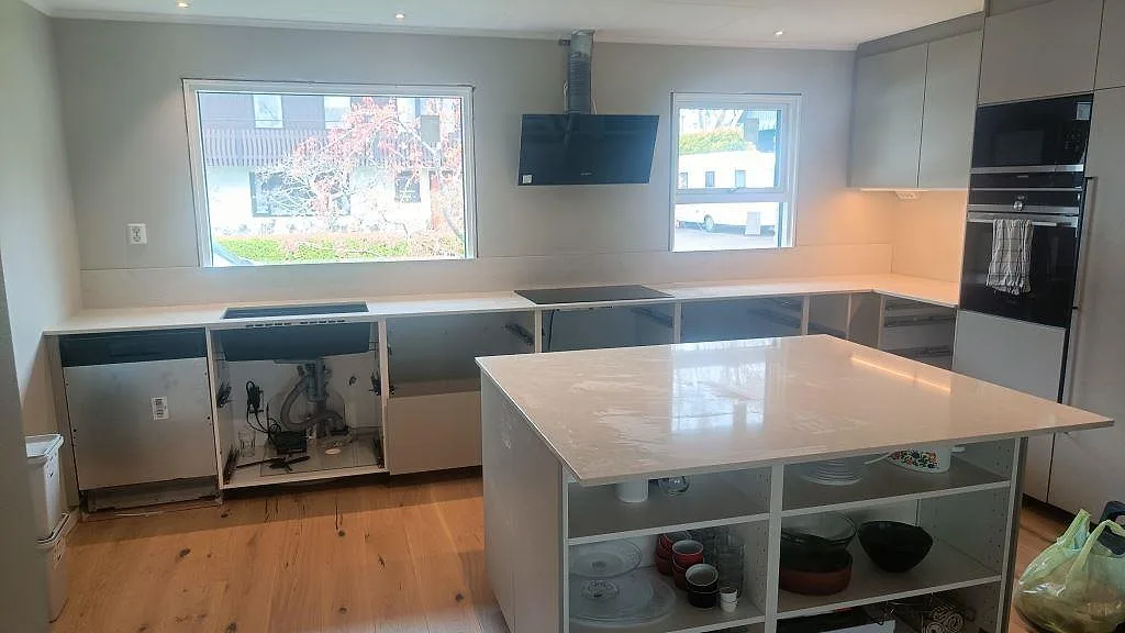 Köksbänkskiva och köksö i polerad Silestone Snowy Ibiza, vit kvartskomposit, med svart häll, svart diskho och stora fönster i Fjärås.