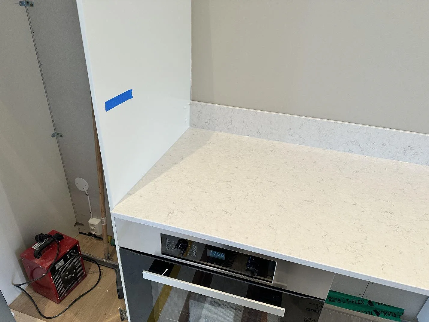 Rak köksbänk i polerad Silestone Snowy Ibiza med 12 mm stänkskydd ovanför inbyggnadsugn under montering i Frillesås.