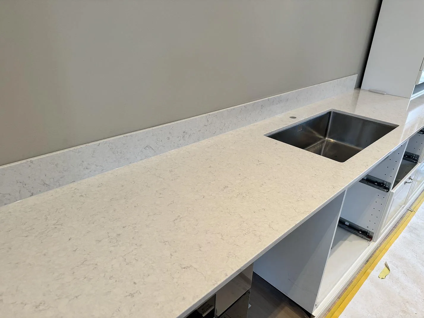 Lång köksbänk i polerad Silestone Snowy Ibiza, vit kompositsten, med underlimmad rostfri diskho och låg stänkkant i Frillesås.