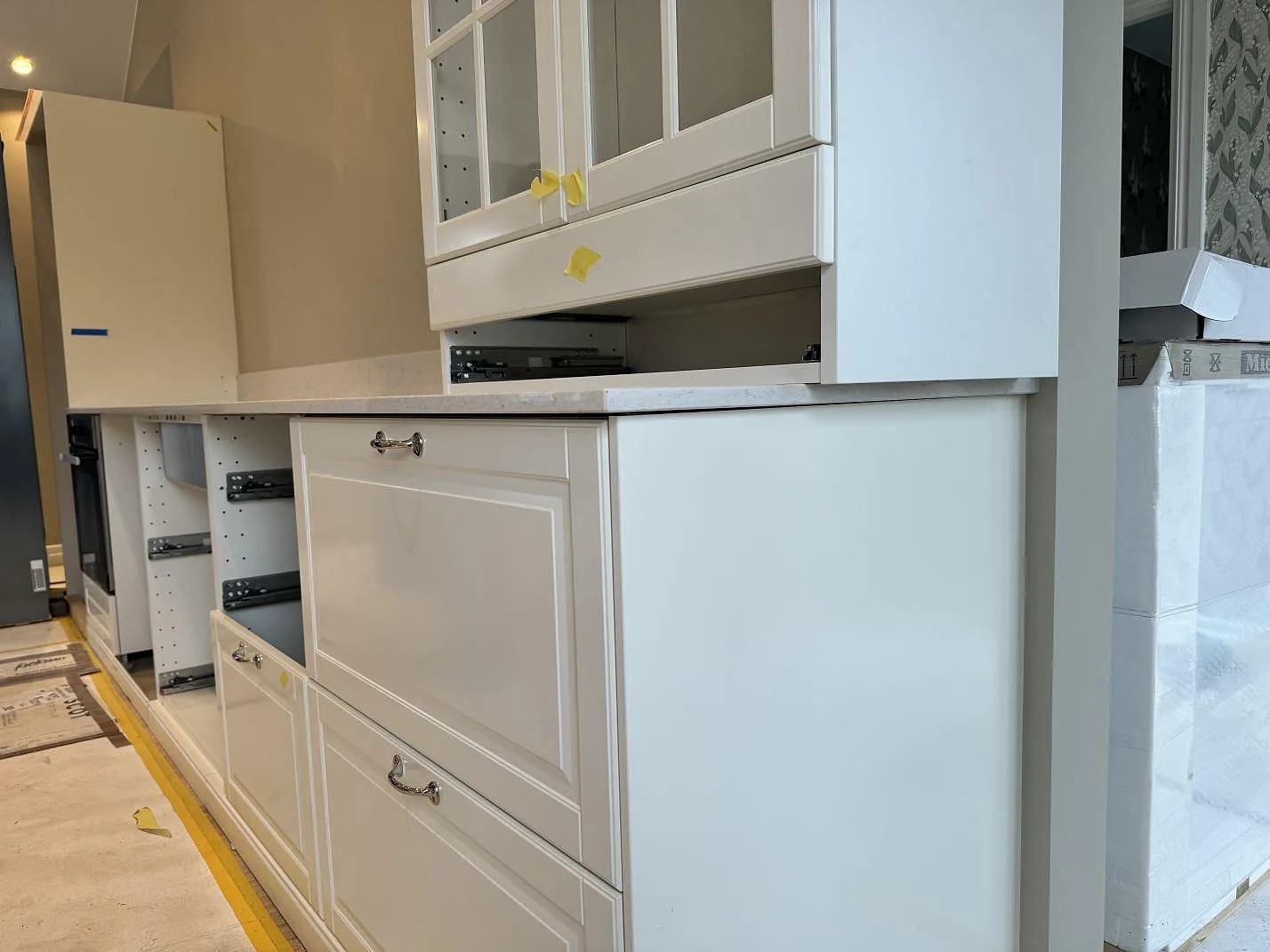 Sidovy av vit köksinredning med polerad Silestone Snowy Ibiza som bänkskiva och stänkskydd under montering i Frillesås.