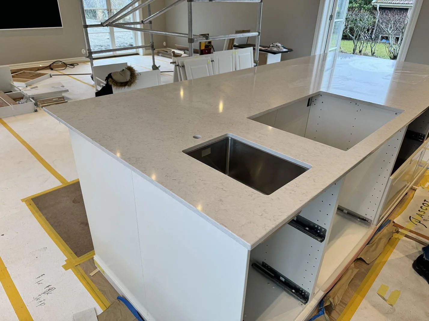 Köksö i polerad Silestone Snowy Ibiza, vit kvartskomposit, med underlimmad rostfri diskho och hällöppning i ett kök i Frillesås.