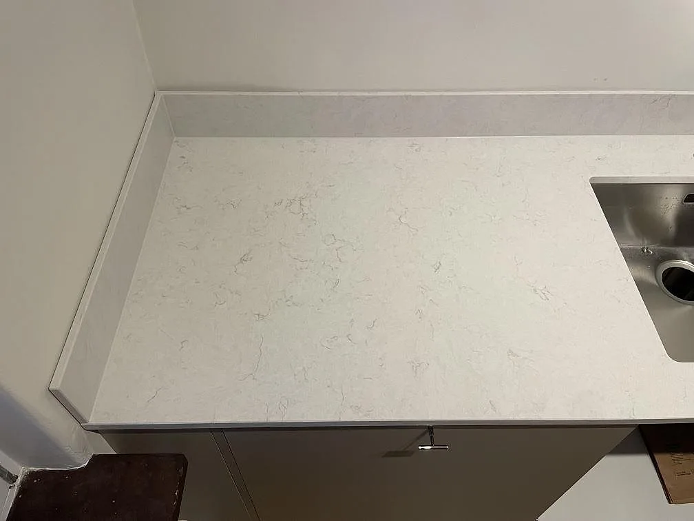 Närbild av polerad Silestone Snowy Ibiza som köksbänkskiva med låg stänkkant och rostfri diskho i Gävle.