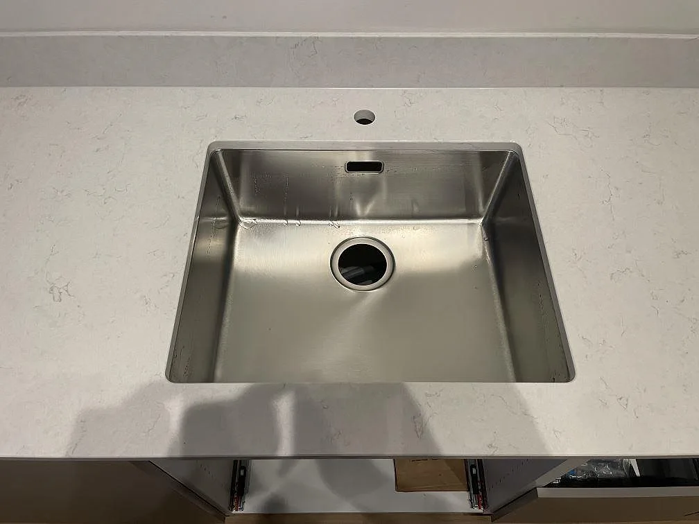 Rostfri diskho monterad i en polerad köksbänkskiva av Silestone Snowy Ibiza med 12 mm stänkskydd i Gävle.