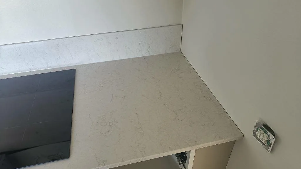 Köksbänkskiva i Silestone Snowy Ibiza i hörn med uppvikt stänkkant och induktionshäll under montering i Gislaved.