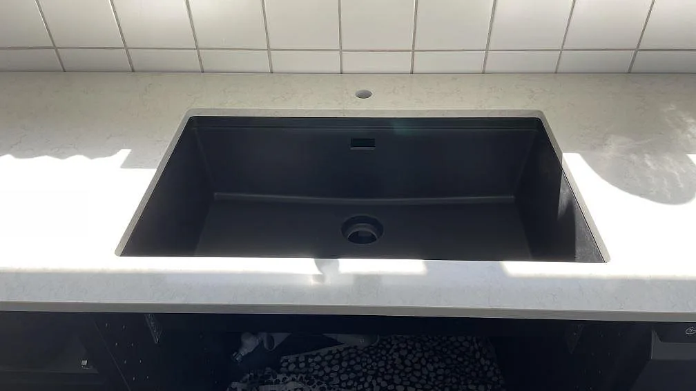 Underlimmad svart kompositho med separat blandarhål i en polerad Silestone Snowy Ibiza-bänk i ett kök i Glumslöv.