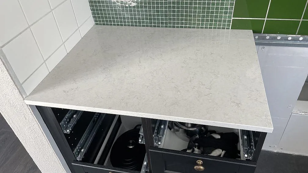 Köksbänkskiva i Silestone Snowy Ibiza ovanpå en mörk lådhurts mot grönt mosaikstänkskydd i ett kök i Glumslöv.
