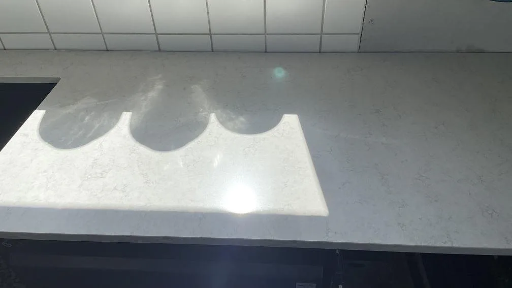 Polerad Silestone Snowy Ibiza-bänk med infälld flaskställning för tre flaskor och fin grå ådring i ett kök i Glumslöv.