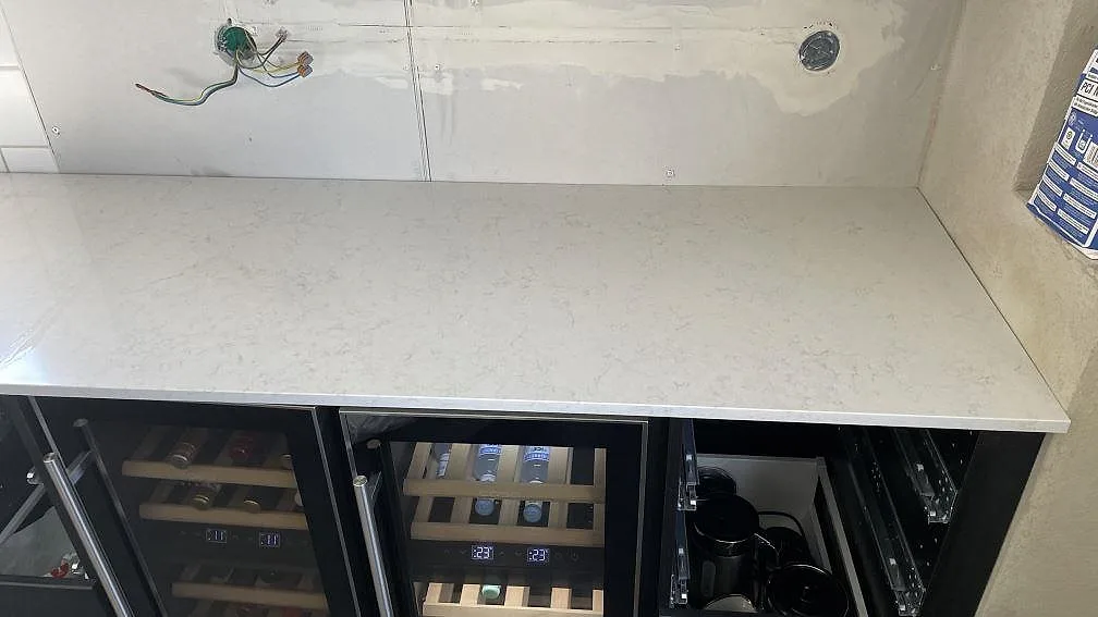 Köksbänkskiva i vit Silestone Snowy Ibiza, polerad, monterad över en rad vinkylar i ett kök under montering i Glumslöv.