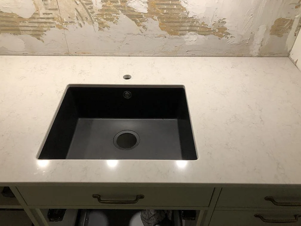 Hörn av köksbänkskiva i vit Silestone Snowy Ibiza, polerad, med nedsänkt mörk diskho och salviagröna stommar i ett kök i Göteborg.