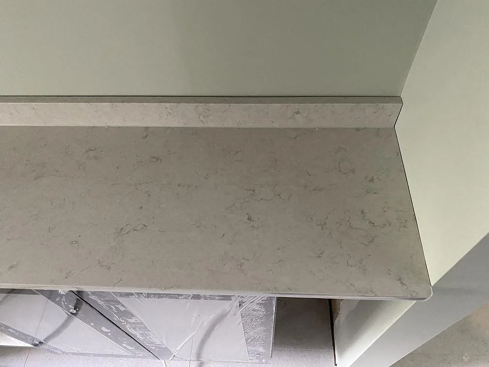 Köksbänkskiva i vit Silestone Snowy Ibiza med uppvikt stänkkant längs salviagrön vägg i ett kök i Göteborg.