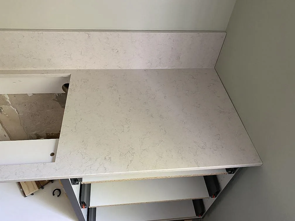 Köksbänkskiva i vit Silestone Snowy Ibiza med grå ådring och uppvikt stänkkant i ett kök under montering i Göteborg.