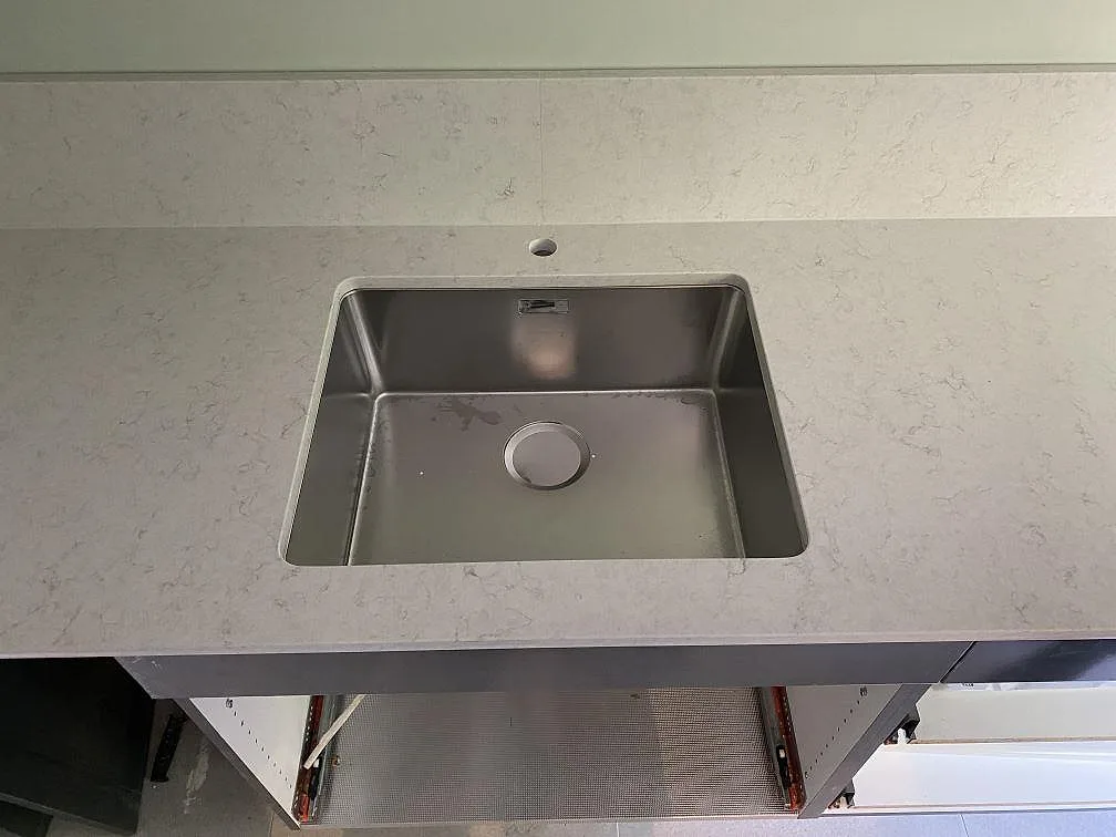 Underlimmad rostfri diskho monterad under en polerad köksbänkskiva i vit Silestone Snowy Ibiza med grå ådring i ett kök i Göteborg.