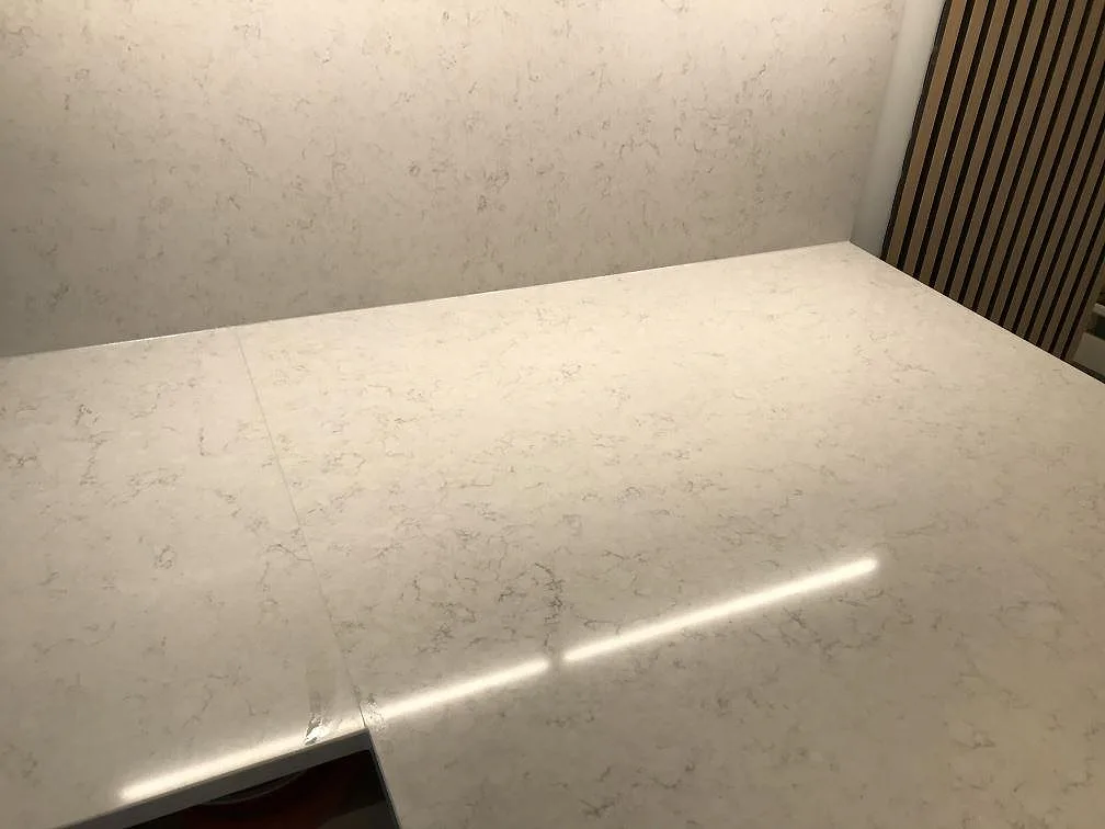 Polerad bänkskiva i Silestone Snowy Ibiza med uppvikt stänkskydd och synlig skarv mot en vägg i träribbor, kök i Göteborg.