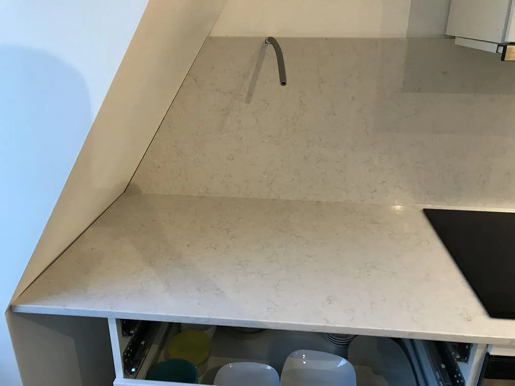 Polerad bänkskiva i Silestone Snowy Ibiza vid en öppen lådstomme under montering, med kanten av induktionshällen synlig, kök i Göteborg.