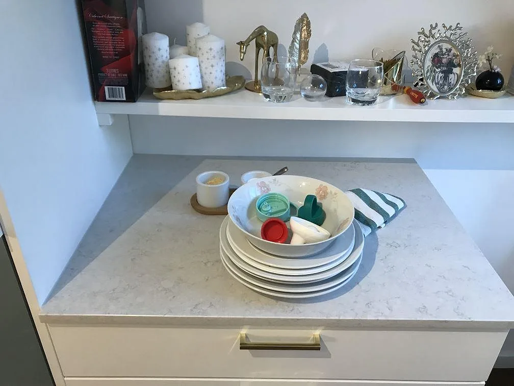 Hörn av polerad köksbänkskiva i vit Silestone Snowy Ibiza med fin grå ådring och vit lucka med mässingshandtag, kök i Göteborg.