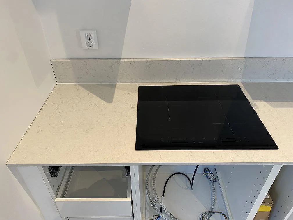 Polerad köksbänkskiva i Silestone Snowy Ibiza i Göteborg med infälld induktionshäll och uppvikt stänkkant i samma sten.