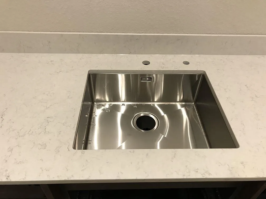 Underlimmad rostfri diskho i polerad Silestone Snowy Ibiza med två borrade hål för blandare i ett kök i Göteborg.