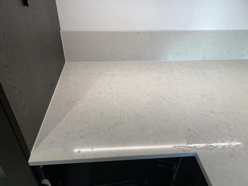 Närbild på polerad Silestone Snowy Ibiza bänkskiva och stänkskydd med skyddsfilm kvar under montering i ett kök i Göteborg.