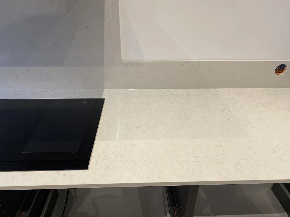 Detalj av polerad Snowy Ibiza halvö i Göteborg med infälld häll och diskret grå ådring i den vita kvartskompositen.