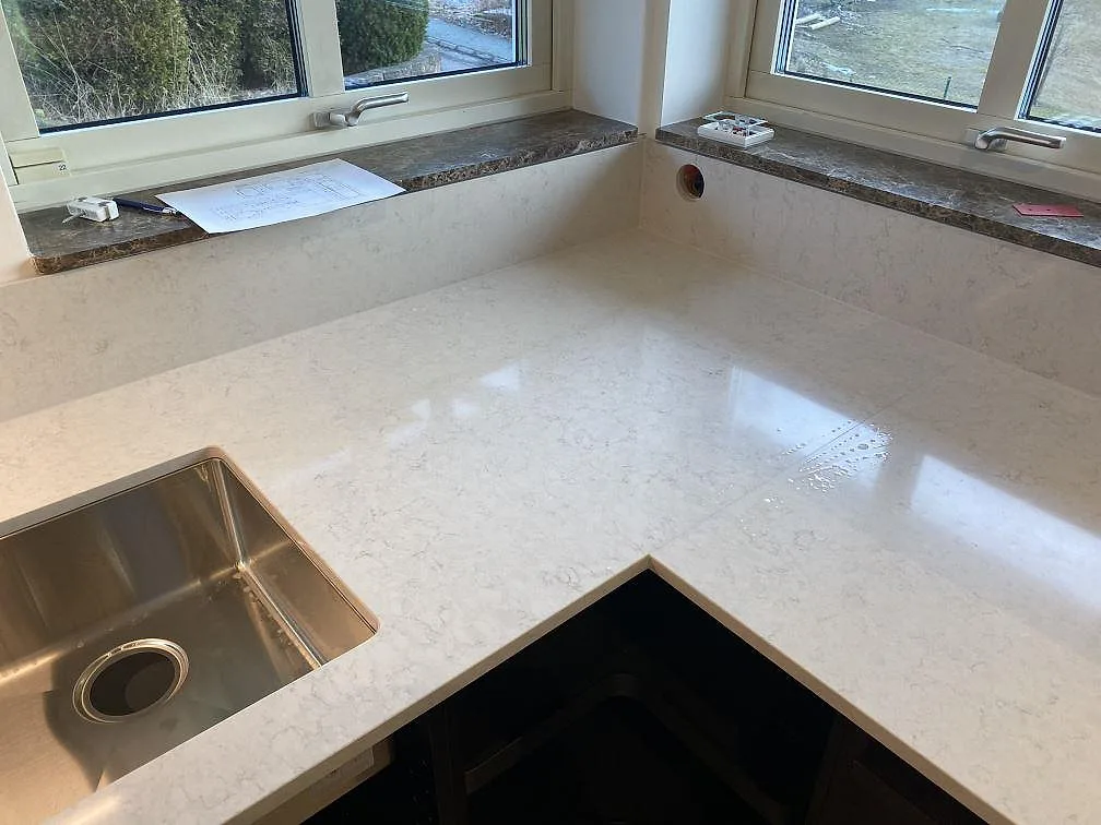 Köksbänkskiva i vit Silestone Snowy Ibiza, polerad, med underlimmad rostfri diskho och uppvikt stänkkant i ett L-format kök i Göteborg.