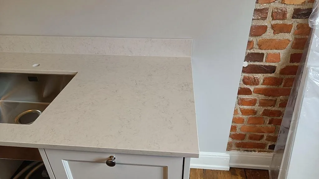 Hörn av bänkskiva i Silestone Snowy Ibiza med underlimmad rostfri diskho intill en frilagd tegelvägg i ett kök i Göteborg.