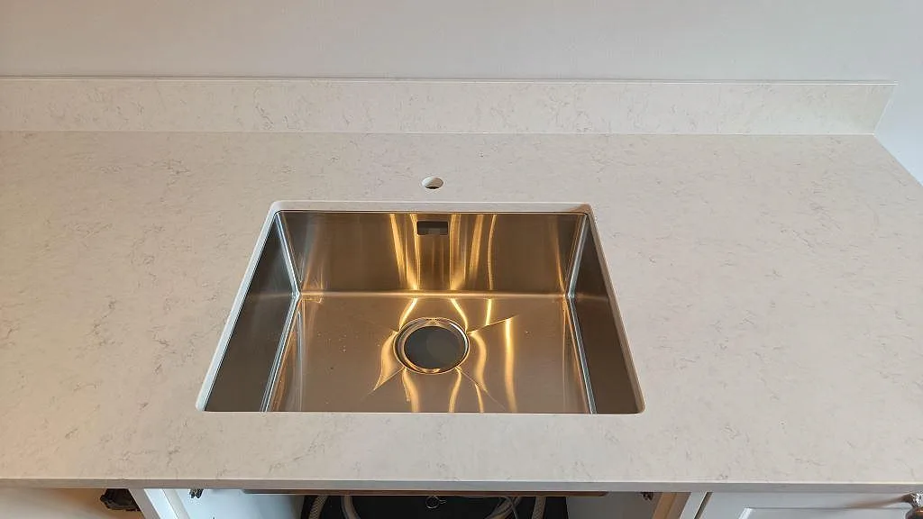 Underlimmad rostfri diskho i en polerad Silestone Snowy Ibiza bänkskiva med borrat hål för blandare i ett kök i Göteborg.