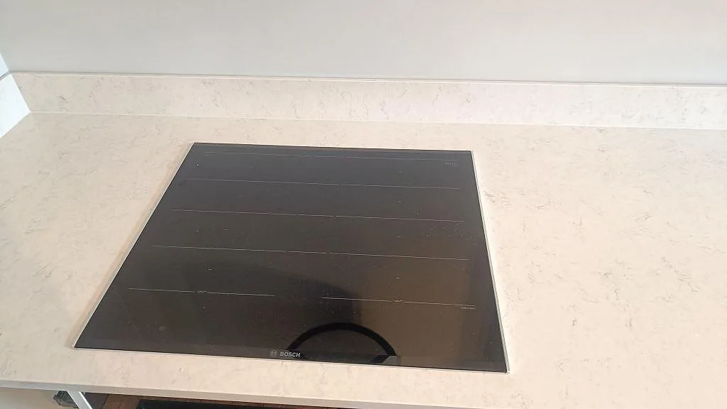 Infälld Bosch induktionshäll i en polerad bänkskiva i Silestone Snowy Ibiza med uppvikt stänkkant i ett kök i Göteborg.