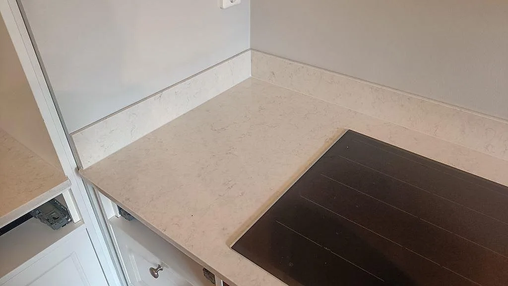 Polerad bänkskiva i Silestone Snowy Ibiza med uppvikt stänkkant i hörnet och infälld häll i ett kök i Göteborg.