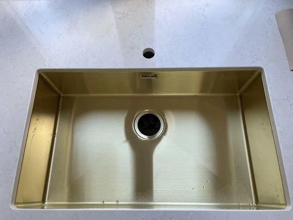 Detalj av mässingsfärgad underlimmad diskho i polerad Silestone Snowy Ibiza komposit i ett kök i Göteborg.