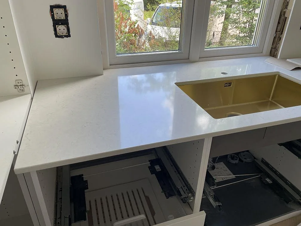 Polerad Silestone Snowy Ibiza köksbänkskiva i komposit under stora fönster med mässingsfärgad diskho i Göteborg.