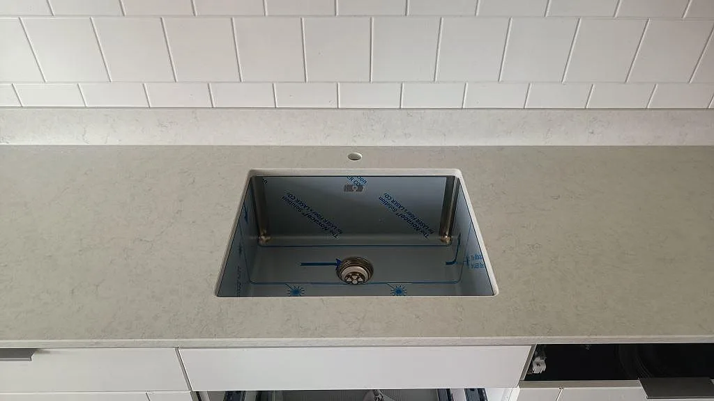 Underlimmad rostfri diskho i en polerad Silestone Snowy Ibiza köksbänkskiva med låg stänkkant och vitt kakel i Göteborg.