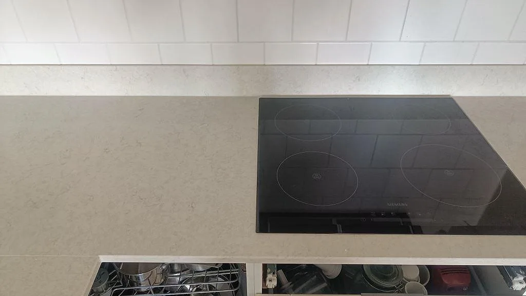 Svart induktionshäll infälld i polerad Silestone Snowy Ibiza kompositbänkskiva med vit köksinredning i Göteborg.