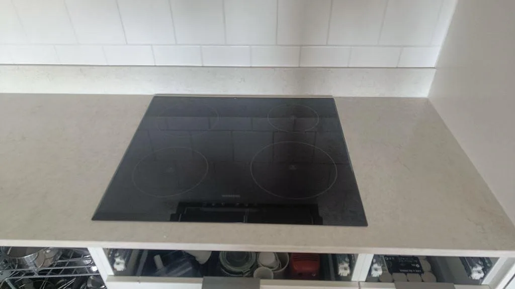 Hällzon i kök med polerad Silestone Snowy Ibiza bänkskiva, låg stänkkant och svart induktionshäll i Göteborg.