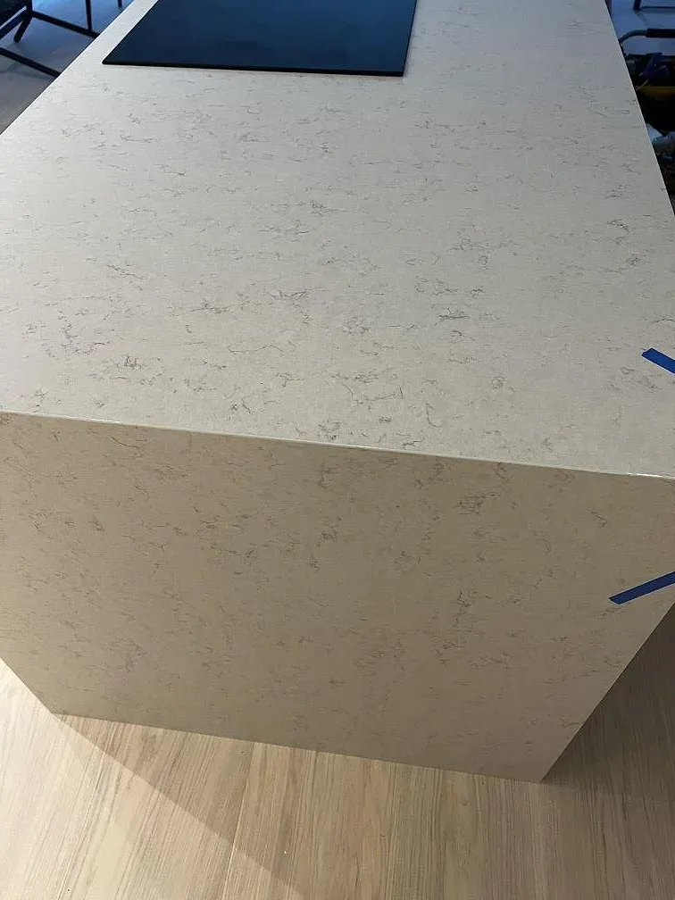 Detalj av köksö i Silestone Snowy Ibiza komposit, Mocka, med mörk häll och tejpade kanter i Göteborg.