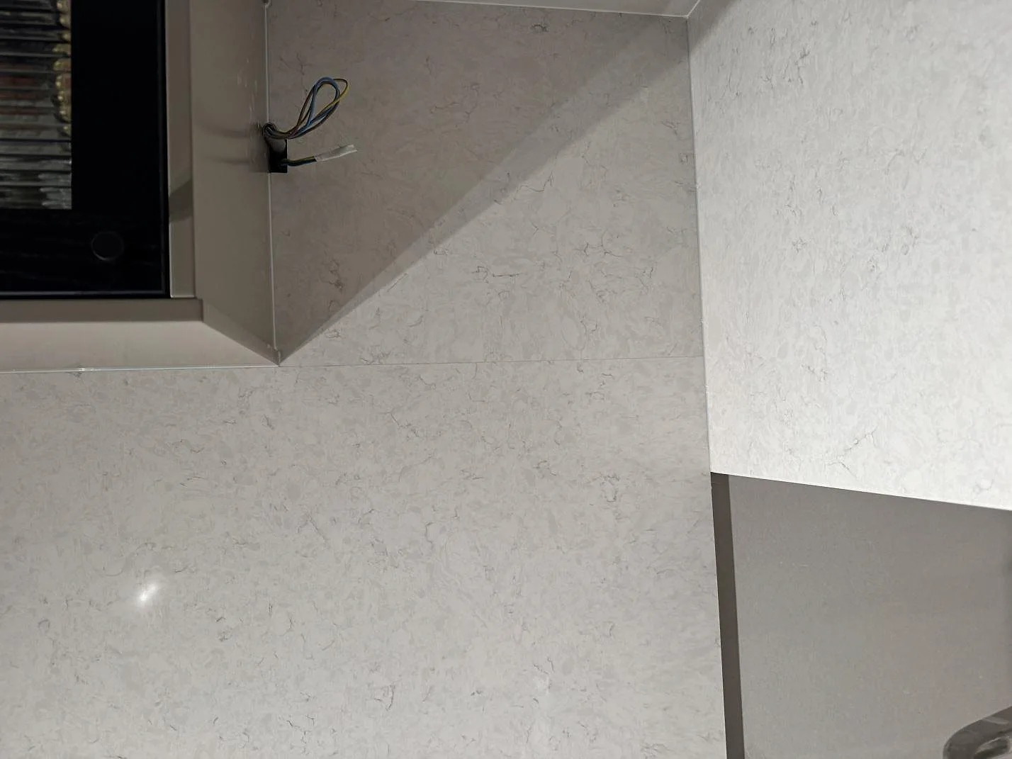 Närbild på polerad väggbeklädnad och bänkskiva i Silestone Snowy Ibiza, kompositsten, intill överskåp i Göteborg.